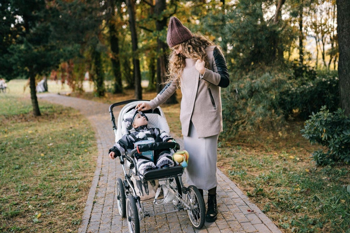 A mother walking with her baby in a pram through a scenic autumn park — a gentle, confident return to movement after birth.