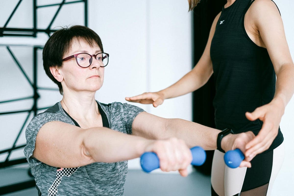 Woman performing resistance training exercise with dumbbells in gym setting, demonstrating strength work for bone health